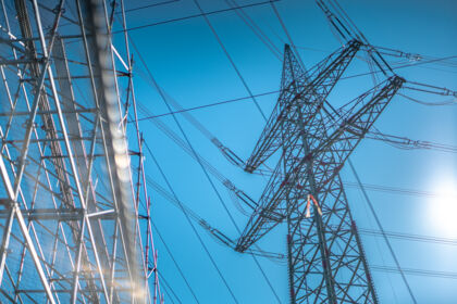 Pyl&ocirc;ne &eacute;lectrique et lignes haute tension sous un ciel bleu clair, symbole de l'infrastructure &eacute;nerg&eacute;tique.